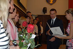 Z lewej strony stoją nauczyciel po ślubowaniu w rękach trzymają kwiaty i akty nominacji. Z prawej prezydent Piotr Grzymowicz wręcza kolejne akty potwierdzające awans