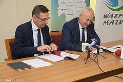 Prezydent Piotr Grzymowicz z lewej i marszałek Gustaw Marek Brzezin z prawej podpisują umowę siedząc przy stole