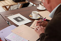 na zdjęciu: senior piszący tekst na kartce papieru