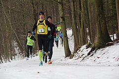 Zawodnicy biegną ośnieżoną leśną ścieżką