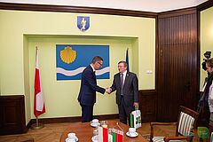 Prezydent Olsztyna i ambasador Białorusi podają sobie ręce na tle flagi Olsztyna